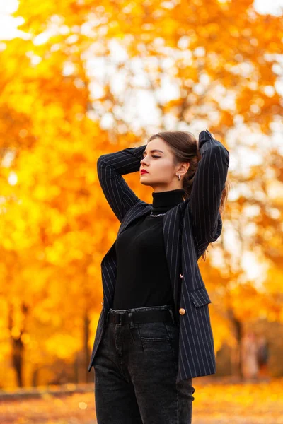 穿着时尚黑色西服 穿着老式毛衣 穿着西装 穿着西装 穿着西装 穿着夹克的时髦漂亮女商人 在秋天落叶的背景下走在户外 — 图库照片