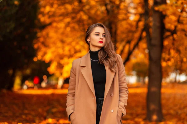 身穿黑色古色古香毛衣 身穿时髦外套 长着红唇的漂亮女孩 落日时分 走在迷人的秋天公园里 有着橙色的树叶 — 图库照片