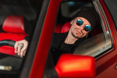 Güneş gözlüklü yakışıklı genç model araba sürüyor.