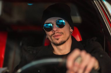Şık güneş gözlüklü genç bir sürücü araba kullanıyor.