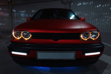 Gece park yerinde yeni LED far optikleri olan havalı kırmızı eski bir araba.