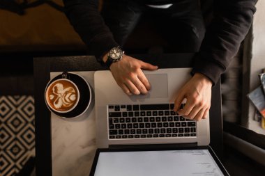 Profesyonel bir adam dizüstü bilgisayarda çalışıyor ve kahve içiyor.