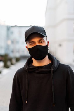 Koruyucu siyah tıbbi maskeli ve şık kapüşonlu şık şapkalı profesyonel bir adam. Dışarıdaki kameraya bakın.
