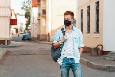 Şık bir kot gömleği ve sırt çantasıyla şehirde gezen, tıbbi maskeli yakışıklı bir adam. Salgın ve koruma