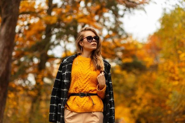 时尚优雅漂亮的女孩 戴着时髦的太阳镜 穿着古旧的黑色外套 黄色针织毛衣 公园里有秋天的五彩斑斓的树叶 — 图库照片