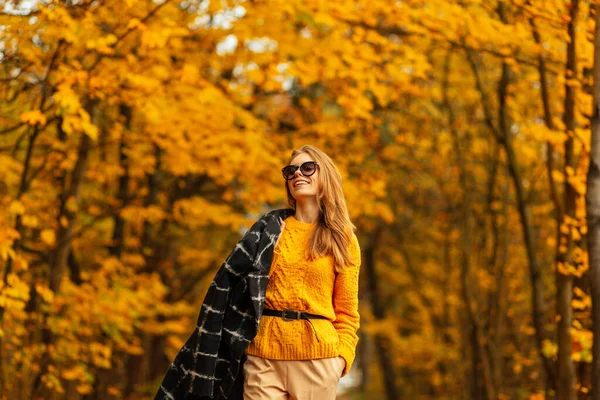 黄色の紅葉が美しい公園を歩いていると お洒落な服に甘い笑顔と感情の表現で幸せな若い女の子 — ストック写真