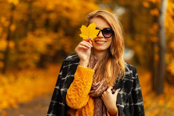 노란색 빈티지 스웨터를 미소를 코트에 선글라스를 소녀와 형형색색의 잎으로 얼굴을 — 스톡 사진