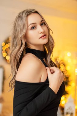 Modadan güzel bir kadın portresi zarif, şık, siyah bir elbise giymiş ve Noel partisinde altın bir arka planda.