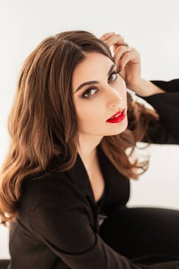 Makyajlı, kırmızı dudaklı, siyah elbiseli ve beyaz arka planda ceketli güzel bir genç kızın portresi.