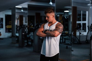 Beyaz tişörtlü, siyah arka planda spor salonunda poz veren yakışıklı bir sporcu.