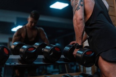 Spor salonunda vücut geliştiren kaslı bir adam. Erkek, saatli güçlü bir el, bir dambıl alır ve bir pazı pompalar.