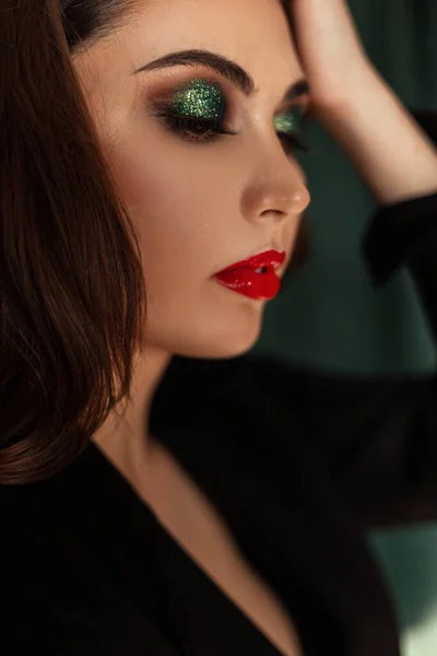 プロの化粧とかなり若い女性モデルのクローズアップ肖像画 緑のヴィンテージの背景にトレンディーな黒の服で赤い唇と緑のアイシャドウ — ストック写真