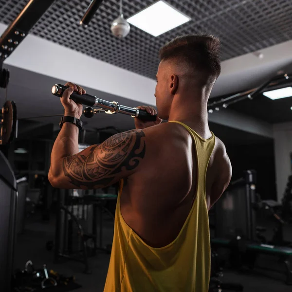 强壮的年轻健美运动员 在健身房的一辆黄色T恤火车上有纹身 — 图库照片