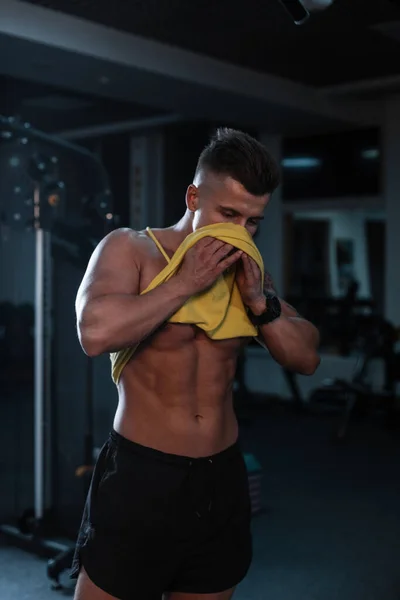 在健身房经过紧张的训练后 肌肉发达的男人用T恤擦拭自己的脸 — 图库照片