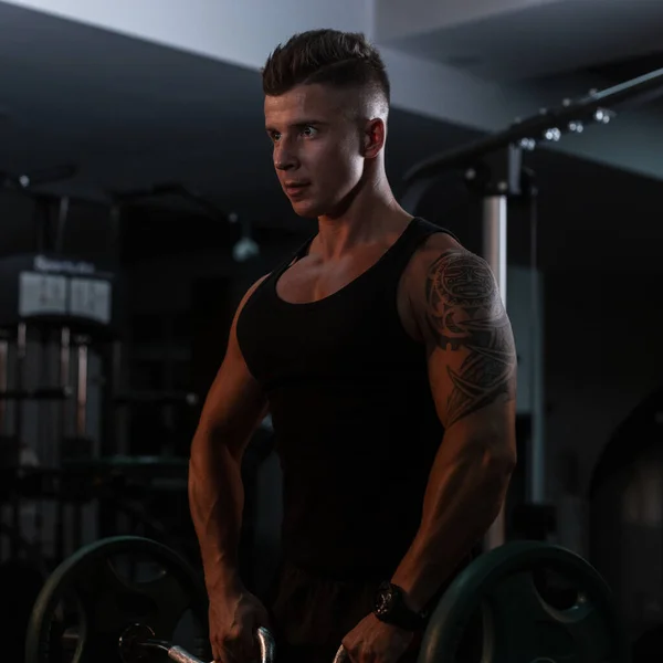 运动健美的男性健美健美运动员 一身肌肉晒黑的身体 肩膀上有梅雅纹身 身穿时髦的黑色T恤 在健身房做运动 — 图库照片