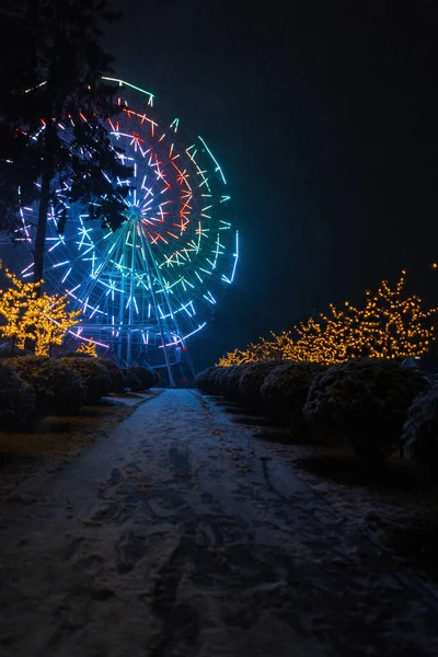 神奇的公园 有一条通向五彩斑斓的摩天轮的路 在冬夜雪天点着灯 大气假日照片 — 图库照片