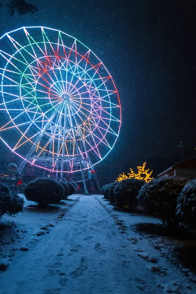 雪地的道路通向迷人的摩天轮 冬天的公园里灯火通明 夜晚白雪连绵 奇幻假期 — 图库照片