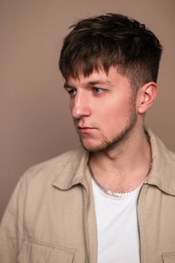 Bej arka planda beyaz tişörtlü, şık ceketli, saç stili yakışıklı bir gencin portresi.