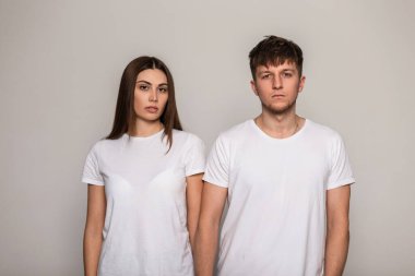 Güzel, şık bir kadın ve stüdyoda gri bir arka planda beyaz tişörtlü yakışıklı, modaya uygun bir adam. Güzellik ve moda