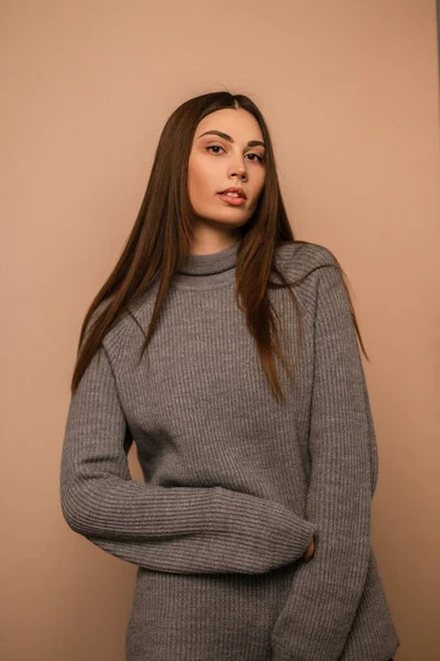 Gri örgü süveter ve bej arka planda güzel, şık bir bayan model. Stüdyoda rahat giyimli bir kız.
