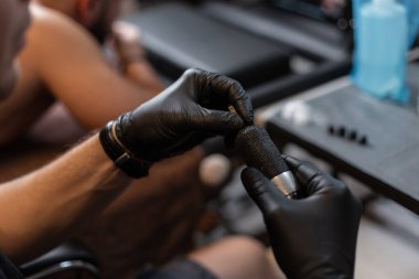 Siyah eldivenli profesyonel dövme sanatçısı yakın plan modern dövme makinesine iğne yapıyor. Dövmeden önce hazırlama işlemi. Dövmeye başla