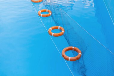 Denizde mavi suda yüzen bir ağ ile turuncu kurtarma çemberleri. Havuzda yardım ve güvenlik. Yaz tatili. Deniz cankurtaranı