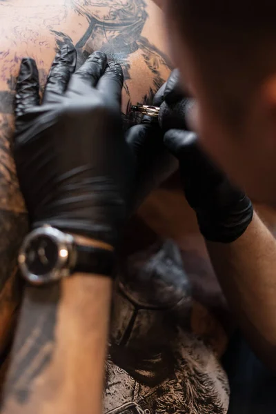 Men\'s hands of a tattoo artist in black gloves with a tattoo machine gets a tattoo on the skin, close-up