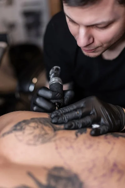 Professional tattoo master man with a tattoo machine stuffs a tattoo on a man\'s back in the studio. Working process