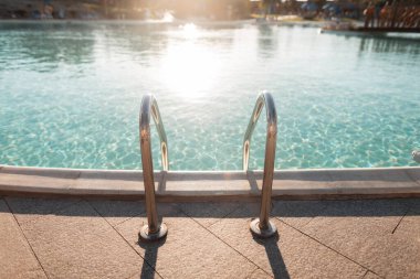 Gün batımında mavi suyu olan güzel bir yüzme havuzu. Havuzdaki metal tırabzanlar. Suya iniş. Yaz tatili, dinlenme ve rahatlama.