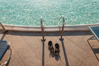 Plaj terlikleri mavi suyu olan bir havuzun yanında ve gün batımında Metal Tırabzan Descent. Yaz tatili, yüzme ve kaplıca.