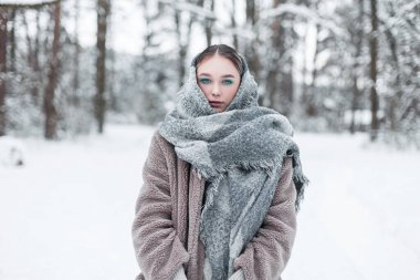 Şık, eski bir eşarp ve kürklü kürklü güzel bir Rus kadın kış ormanında kar altında duruyor.
