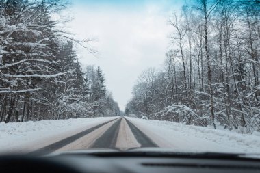 Kış ormanı yakınlarındaki kar manzaralı güzel bir yol. Arabayla yolculuk, arabadan manzara.