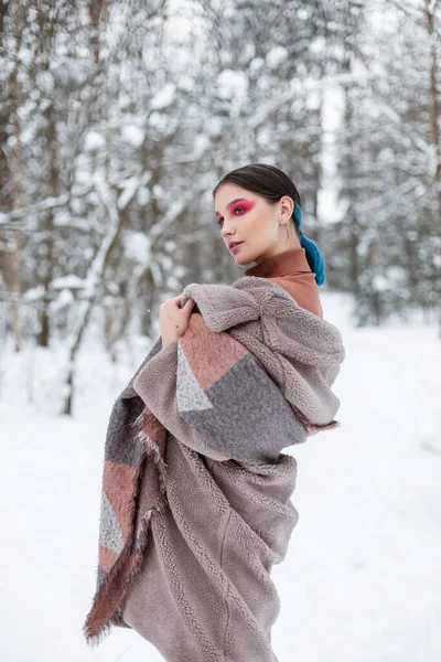 穿着时髦的冬季保暖衣服 头戴围巾 身穿羽绒服的年轻貌美女子站在雪地的树林里 — 图库照片