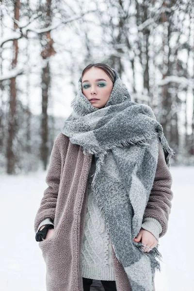 在寒冷的冬日里 身穿时髦外套 头戴老式针织围巾 身穿复古皮衣的俄罗斯年轻貌美的女模特站在森林里 雪地飘扬 — 图库照片