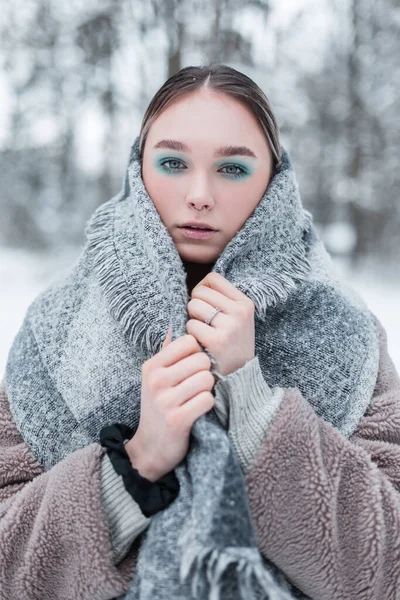 一位年轻的俄罗斯姑娘穿着时髦的冬季服装 戴着老式的温暖围巾 穿着毛皮外套和毛衣 穿着冬装 站在雪地的森林里 她的冬季画像 — 图库照片