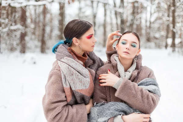 在冬日的公园里 两个穿着冬季时尚服装 头戴彩色彩妆的年轻女郎在雪地里摆姿势 — 图库照片