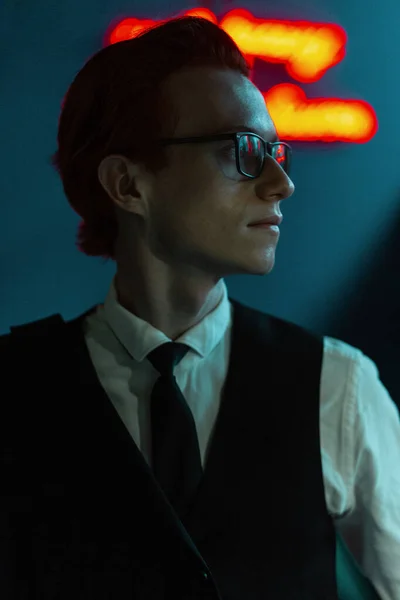ファッションビジネスで眼鏡をかけたハンサムなスタイリッシュな若い男モデルスーツと赤と青の光とバーでネクタイ — ストック写真