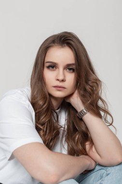 Pretty woman with hairstyle sits in studio on a white background and looks at the camera. Female portrait