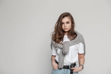 Havalı, modaya uygun bir giysi içinde beyaz tişört ve kot pantolonla şık bir bayan manken beyaz arka planda stüdyoda duruyor. Kadın kıyafeti.