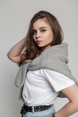 Süveter, t-shirt ve kot pantolon giyen hoş bir kız stüdyoda poz veriyor. Güzel kadın yüzü.