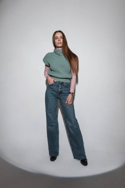 Süslü, eski moda kıyafetler içinde şık bir kadın. Yelek, gömlek ve kot, stüdyoda sert ışıkla poz veriyor.