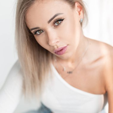 Güzel, narin, genç, sarışın bir kızın portresi. Dudakları ve yeşil gözleri beyaz bir tişörtle beyaz arka planda.