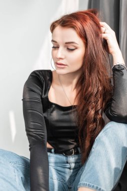 Siyah tişörtlü ve kot pantolonlu güzel bir kız model stüdyoda güneş ışığıyla oturuyor.