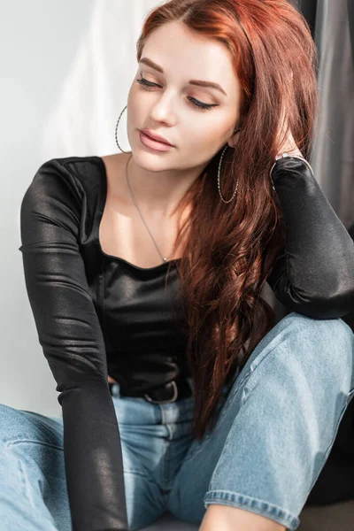 Siyah tişörtlü ve mavi kotlu güzel bir bayan model güneş ışığıyla aynı odada oturuyor..