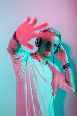 Gözlüklü ve kulaklıklı hippi yakışıklı dansçı müzik dinler ve stüdyodaki pembe ve mavi ışıkla kameraya uzanır..