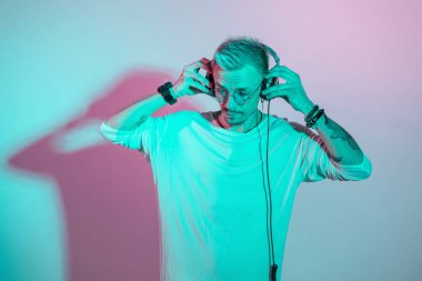 Müzik aşığı hipster gözlüklü adam stüdyoda pembe ve cyan ışığı olan kulaklıkla müzik dinliyor. Yaratıcı erkek portresi