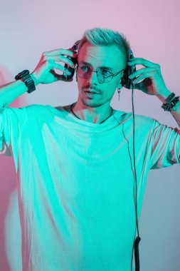 Modaya uygun beyaz tişörtlü yakışıklı manken kulaklıkla pembe ve mavi renkte müzik dinliyor.