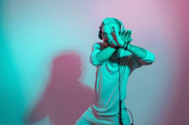Hippi dansçı kulaklıkla müzik dinliyor ve stüdyoda pembe ve mavi ışıkla dans ediyor.