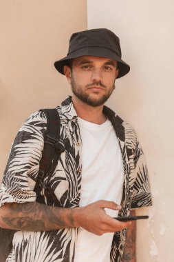 Akıllı telefonlu şık elbiseli yakışıklı, hippi bir turist duvarın yanında duruyor. Erkek gezgin