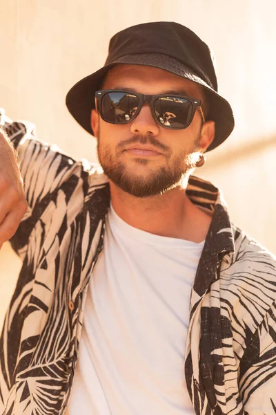 Hipster man with sunglasses in fashion shirt and hat at sunset